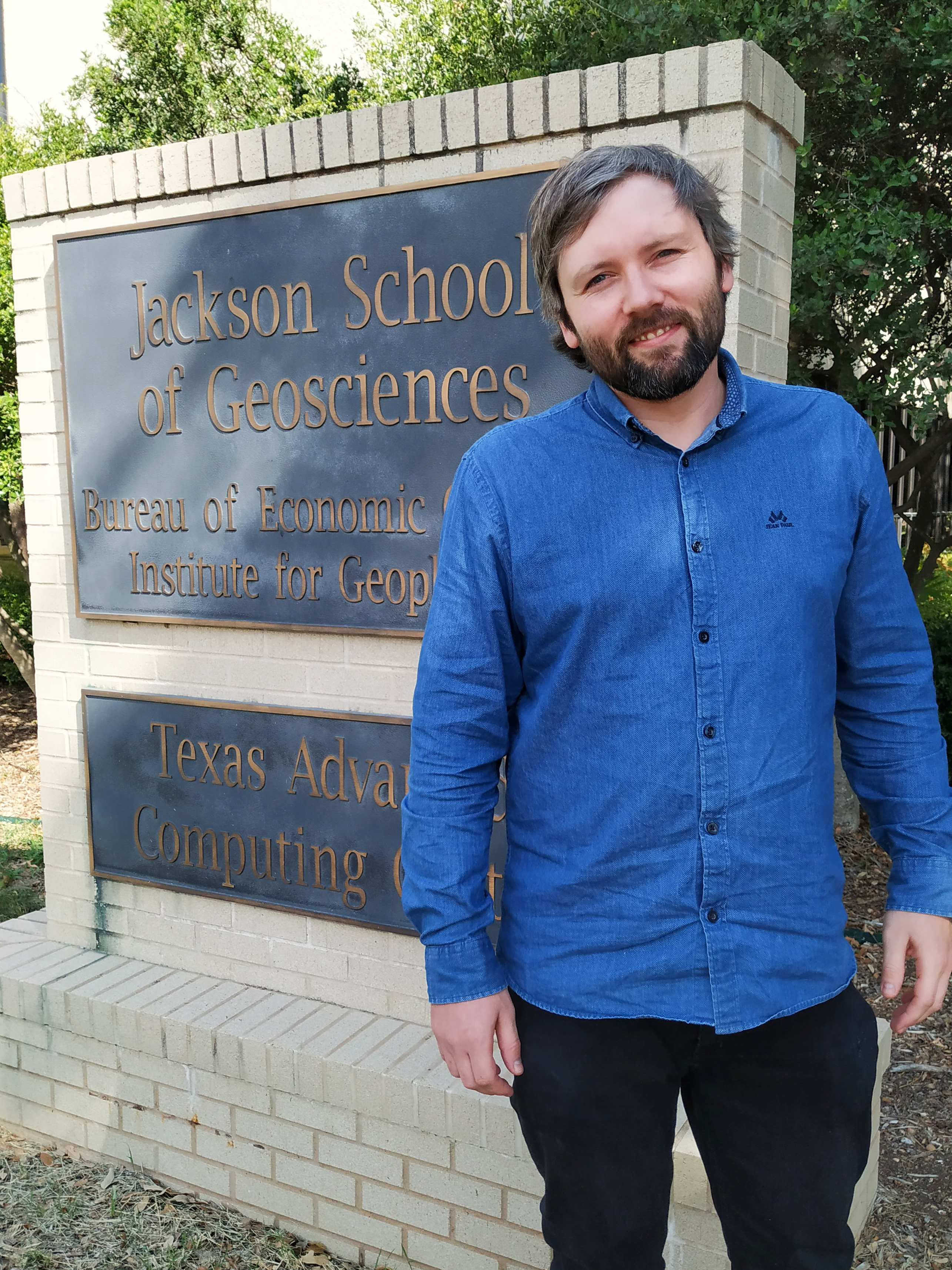 Kristian stands in front of the Jackson School of Geosciences/Bureau of Economic Geology sign in front of the building
